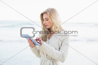 Pensive blonde woman in wool cardigan using a tablet pc