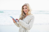 Cheerful blonde woman in wool cardigan using a tablet pc