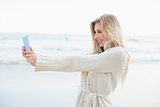Amused blonde woman in wool cardigan taking a picture of herself with a tablet pc