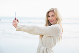 Delighted blonde woman in wool cardigan taking a picture of herself with a tablet pc