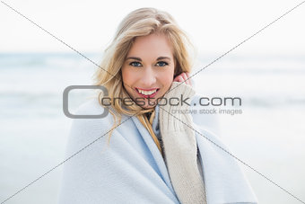 Pleased blonde woman covering herself in a blanket