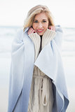 Smiling blonde woman covering herself in a blanket