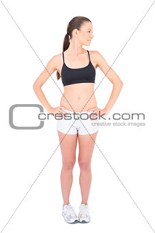 Fit smiling woman in sportswear hands on hips looking away