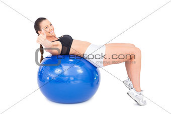 Sporty woman working out with exercise ball giving thumb up to camera