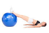 Side view of smiling fit woman lying working out with exercise ball