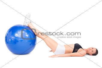 Side view of relaxed fit woman lying working out with exercise ball