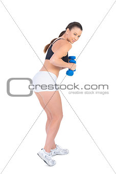 Smiling sporty brunette exercising with dumbbells