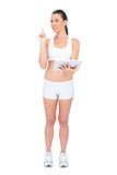 Fit woman in sportswear holding tablet computer pointing up