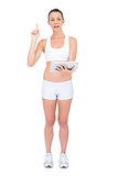 Fit woman in sportswear holding tablet and pointing up