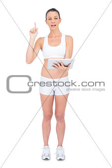 Fit woman in sportswear holding tablet and pointing up