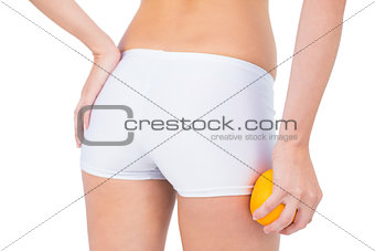 Rear view of fit woman holding orange by her thigh