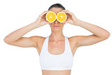 Fit woman holding slices of orange on her eyes