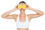Smiling fit woman holding slices of orange on her eyes