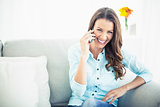 Attractive model sitting on cosy couch having a phone call
