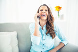 Smiling model sitting on cosy couch having a phone call
