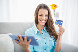 Smiling woman holding tablet and showing her credit card