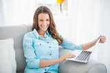 Smiling woman holding laptop sitting on couch