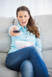 Doubtful woman sitting on sofa changing tv channel