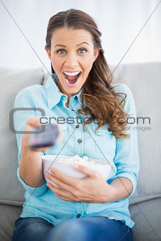 Surprised woman sitting on sofa changing tv channel