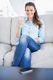 Smiling woman holding water glass sitting on sofa
