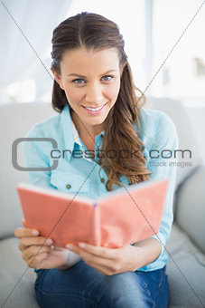 Smiling woman sitting on sofa reading book