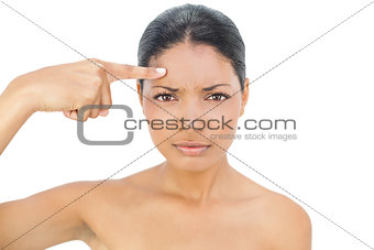 Frowning black haired model pointing at her forehead