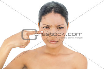 Frowning black haired model pointing at her cheek