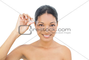 Cheerful black haired model removing hairs from her eyebrow