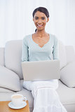 Cheerful attractive woman using her laptop sitting on cosy sofa