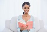 Smiling attractive woman sitting on cosy sofa reading a book