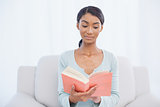 Pensive attractive woman sitting on cosy sofa reading a book