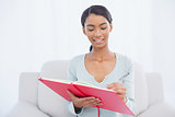 Smiling attractive woman sitting on cosy sofa writing