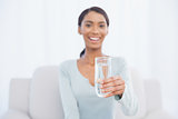 Smiling attractive woman sitting on cosy sofa holding glass of water
