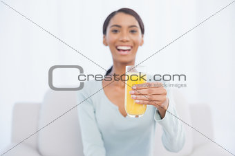 Smiling woman sitting on cosy sofa holding glass of orange juice