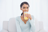 Smiling woman sitting on cosy sofa drinking orange juice