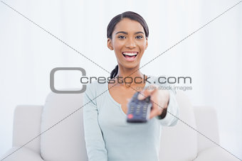 Smiling woman sitting on sofa changing tv channel