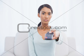Serious woman sitting on sofa changing tv channel