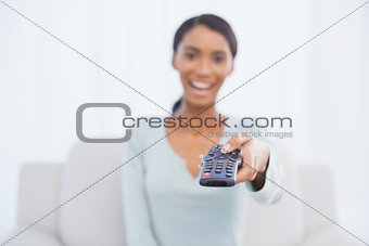 Cheerful woman sitting on sofa changing tv channel
