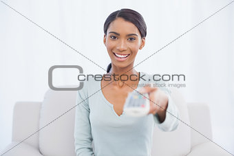 Cheerful cute woman sitting on sofa changing tv channel