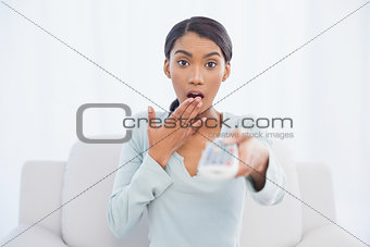 Shocked cute woman sitting on sofa changing tv channel