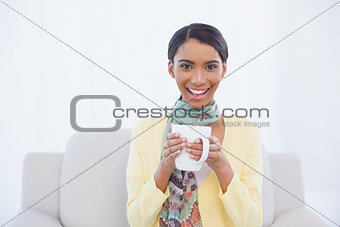 Smiling pretty woman sitting on sofa holding mug of coffee
