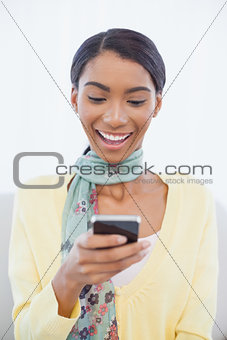 Smiling elegant woman sitting on sofa text messaging