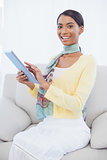 Smiling elegant woman sitting on sofa using her tablet