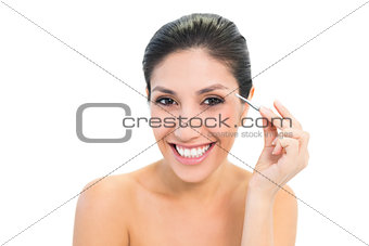 Brunette plucking her eyebrows and smiling at camera