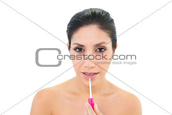 Brunette applying lip gloss and looking at camera