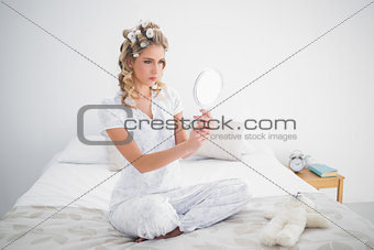 Serious blonde looking at reflection on cosy bed