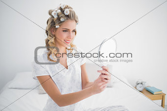 Smiling blonde looking at reflection on cosy bed