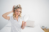 Cheerful gorgeous blonde wearing hair curlers holding mirror
