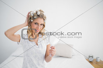 Cheerful gorgeous blonde wearing hair curlers holding mirror