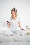 Smiling pretty blonde wearing hair curlers text messaging